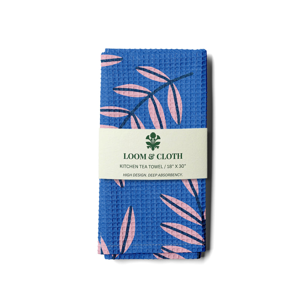 Blue kitchen towel with pink leaf pattern and Loom & Cloth label on a white background