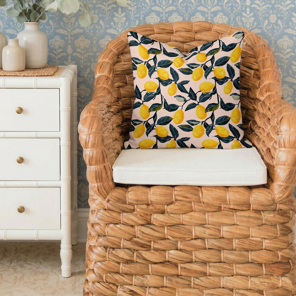 Wicker chair with a decorative square pillow featuring Lemon Pink pattern in a room with floral wallpaper.