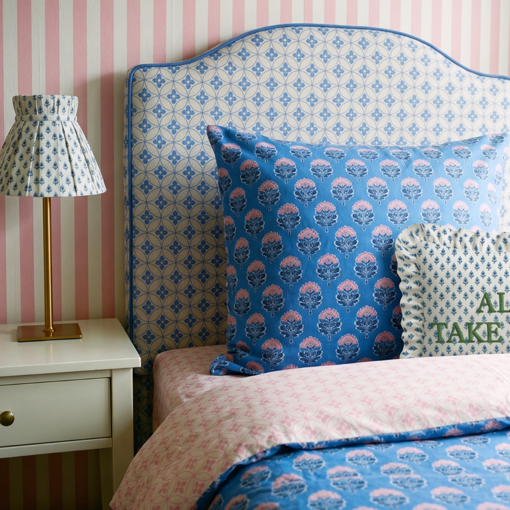 Bedroom with patterned headboard, pillows, and lamp against striped pink and withe wall.