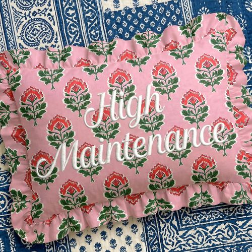 Pink floral pillow with 'High Maintenance' text on a blue and white patterned background